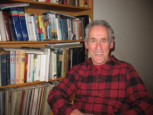 Professor Joe Butwin smiles in his office, seated in front of a bookshelf full of books