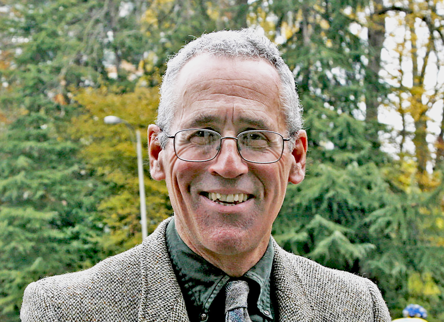 Joe Butwin smiles at the camera in suit and glasses, in front of trees