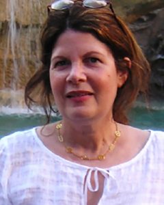 Picture of Susan Glenn smiling outdoors, wearing a white blouse, with a body of water in the background