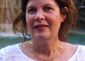 Picture of Susan Glenn smiling outdoors, wearing a white blouse, with a body of water in the background
