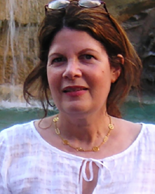 Susan Glenn smiling outdoors, wearing a white blouse, with a body of water in the background