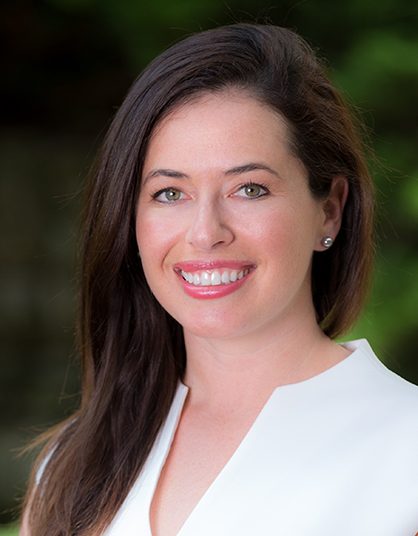 Sarah Zaides Rosen smiling, wearing white blouse with greenery in background