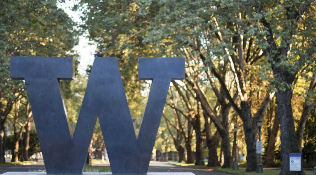Photo of bronze sculpture of a "W" at an entrance to the University of Washington. Leafy trees are visible in the background.