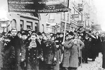 Workers march down the street carrying a banner covered with Yiddish slogans