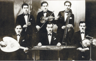 A historic photograph of a group of mustachioed musicians in suits, holding a combination of Western and traditional instruments
