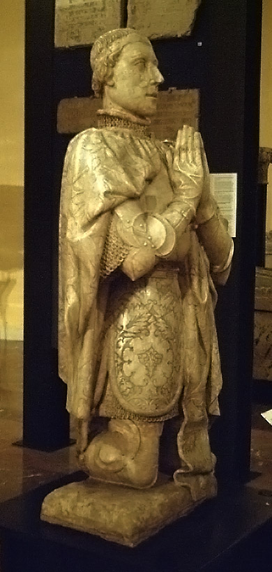A shining statue depicts a pious king in royal garb on his knees, hands folded in prayer in front of him