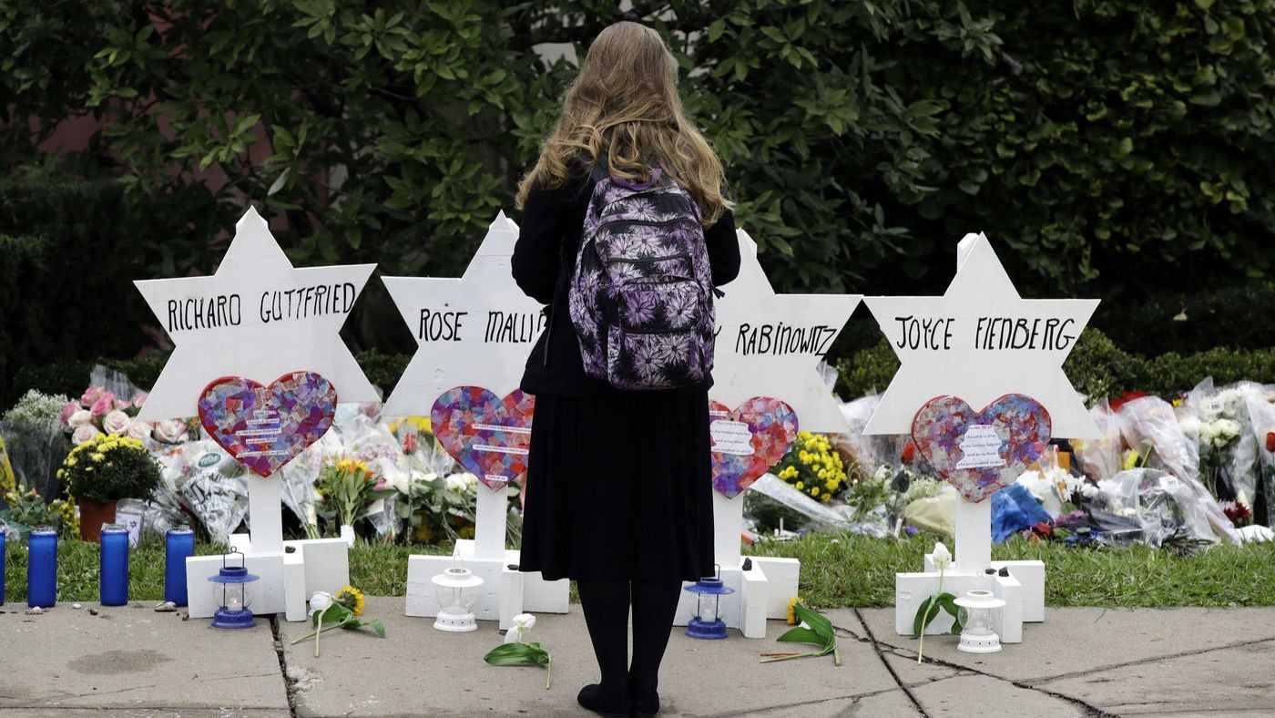 Woman in black, wearing a backpack stands in front of markers bearing the names of synagogue shooting victims