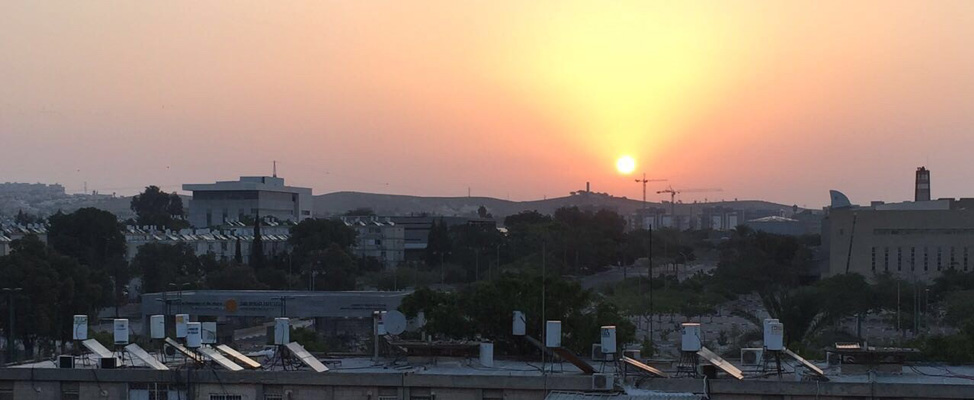 A photo of Beer Sheva at dawn, showing the sun shining pink through smog just above the horizon