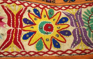 A colorful embroidered cloth with a flower-like yellow starburst surrounding a crescent moon in the middle and red and purple floral pattern on either side