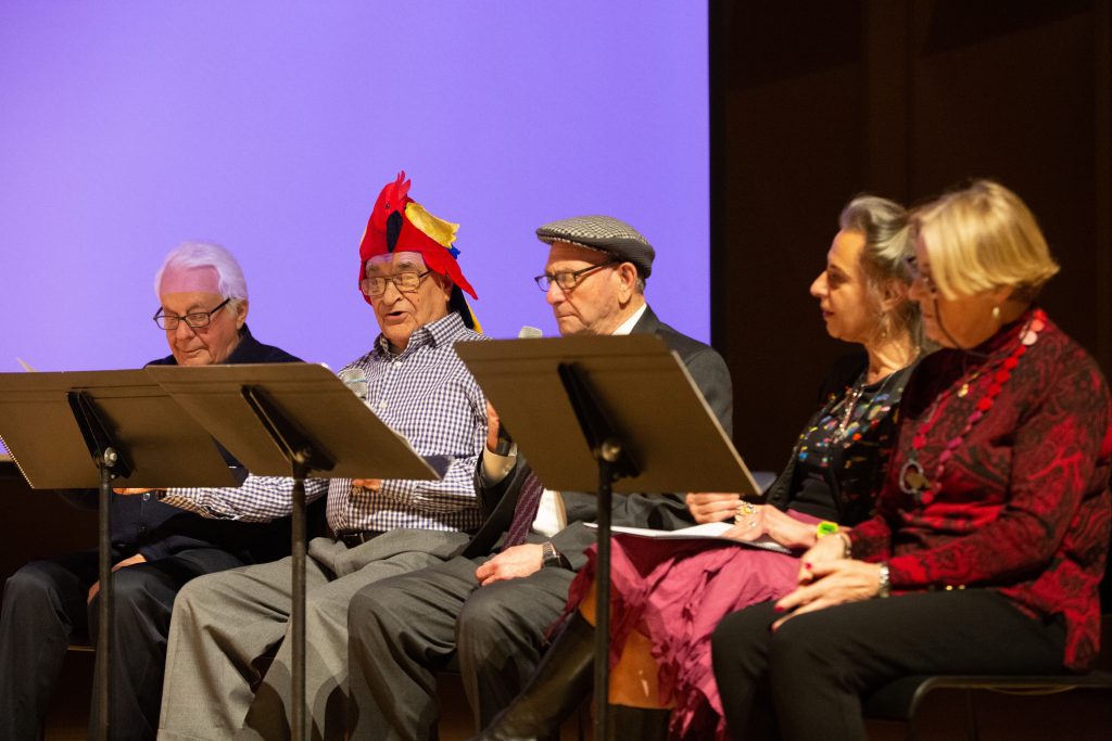 Members of the Ladineros group, including one man wearing a parrot hat, read from scripts
