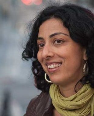 Portrait of Ayelet Tsabari smiling, wearing a scarf, leather jacket, and earrings