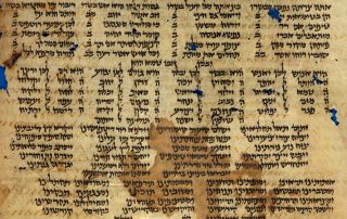 An ancient calfskin manuscript covered in columns of Hebrew writing, showing visible signs of age through discoloration, spotting and missing pieces.