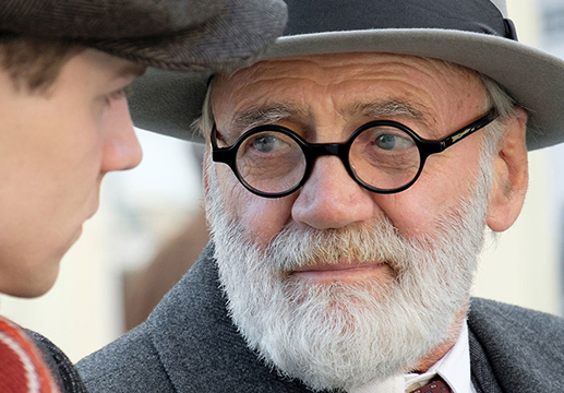 Film still showing actor Bruno Ganz as Sigmund Freud, wearing round spectacles, a hat and coat