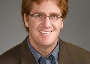 Portrait of Joel Walker in button-up shirt and blazer, with a gray studio background