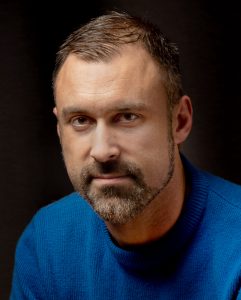 Studio portrait of Nick Barr wearing a sweater, looking serious