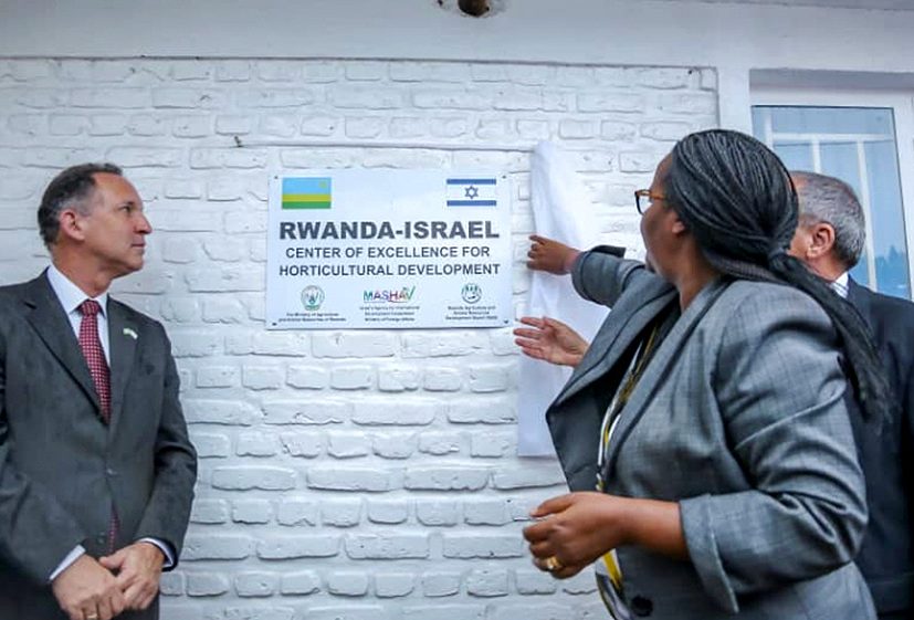 Gil Haskel, wearing a suit and tie, stand alongside a sign reading "RWANDA-ISRAEL Center of Excellence for Horticultural Development" with Minister Mukeshimana in suit and another official gesturing towards it