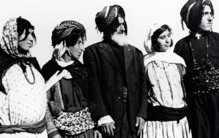 A black-and-white photograph of family members standing in a line, wearing traditional clothing: robes, turbans with tassels and headscarves