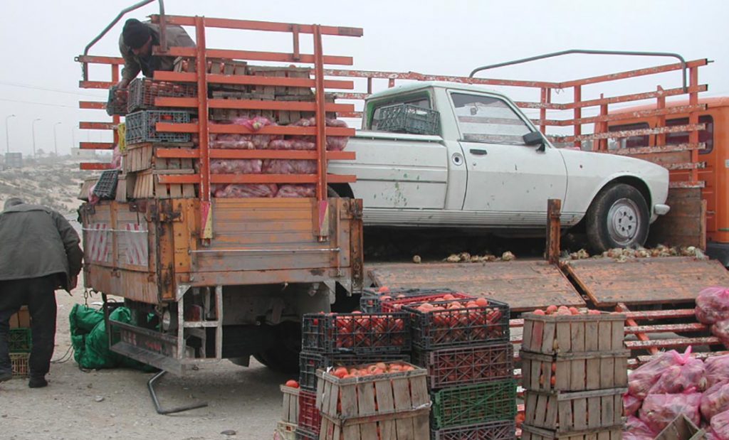 A white truck sitting in an open trailer, with stacked crates of apples on the side