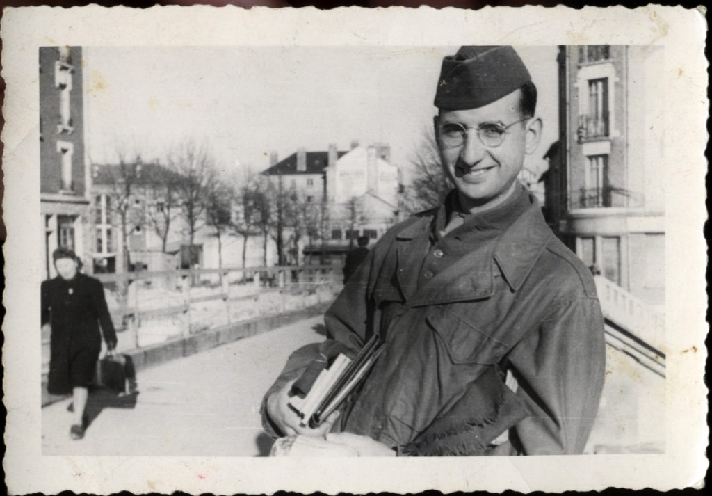 Black and white photo of David Romey smiling wearing military garb and holding books.