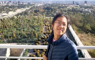 Wendi Zhou smiling, outdoors, a desert city skyline in the background