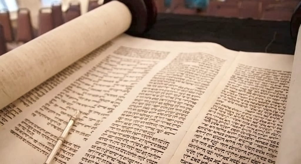 Torah scroll unfurled, showing dense Hebrew writing and a metal yod (pointer)
