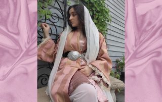 Mirushe Zylali wears traditional Balkan clothes: a pink silk robe with a silver belt and white head covering.