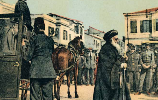 Postcard depicting the chief rabbi of Salonica walking through the streets, and a man tending to his horse. Cityscape in background.