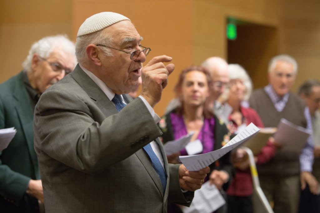 Isaac Azose in the foreground leading a singing group, pictured in the background.