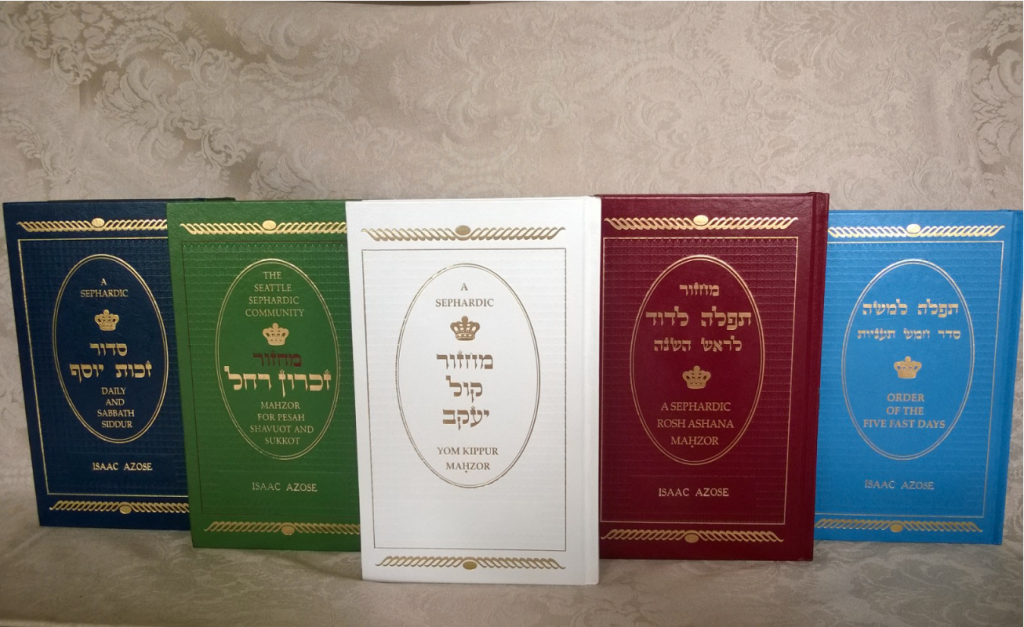 Prayerbooks published by Hazzan Isaac Azose lined up, standing. Left to right: blue book, green book, white book, red book, turquoise book.