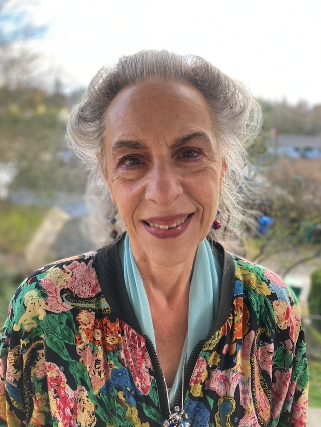 Marlene Souriano-Vinikoor wearing a floral shirt and blue scarf. Trees in the background.