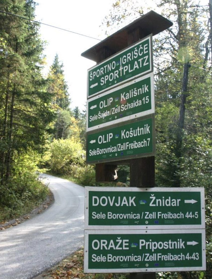 Multiple road signs showing place names listed in German and Slovenian