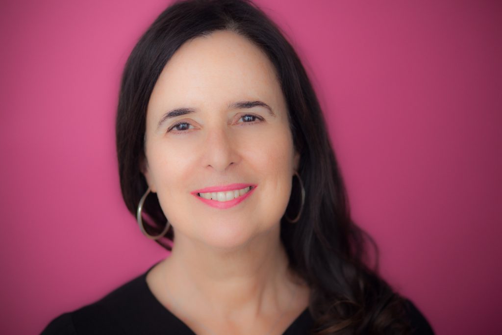 Headshot of Ruth Behar against a pink background.