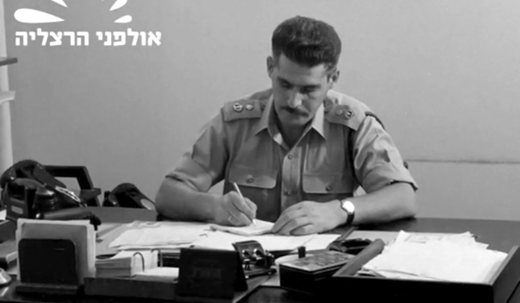 Black and white footage showing a man in military uniform filling out paperwork at a desk in his office