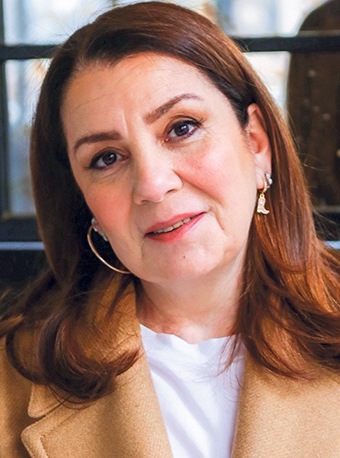 Headshot of Rana Denizer. She is wearing a beige trench coat and a white t-shirt. Her hair is auburn colored and her head is tilted toward the left of the screen.