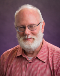 Headshot of James Felak. He has a white beard and is wearing a pink shirt. The backdrop is purple. He is wearing glasses.