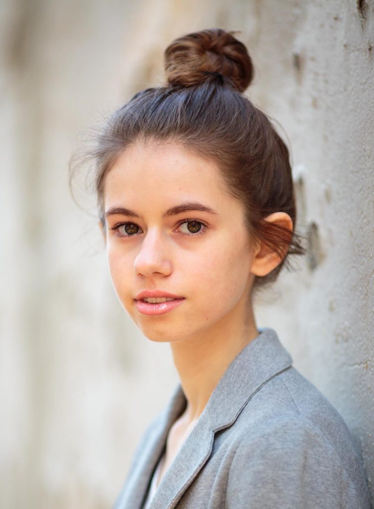 Headshot of Lauren Zarlingo. She has brown hair that's pulled up in a bun. She is wearing a light blue blazer. The Background is grey concrete.