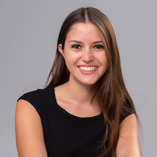 Portrait of Dafne Beri. She is wearing a black tshirt and has brown hair. She is smiling. The background is grey.