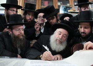 Traditionally dressed Hasidic men around a rabbi writing a Torah scroll