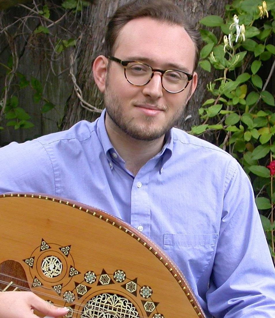 Asher Levy smiling and playing Arabesque string instrument with a tree, leaves, and flowers in the background