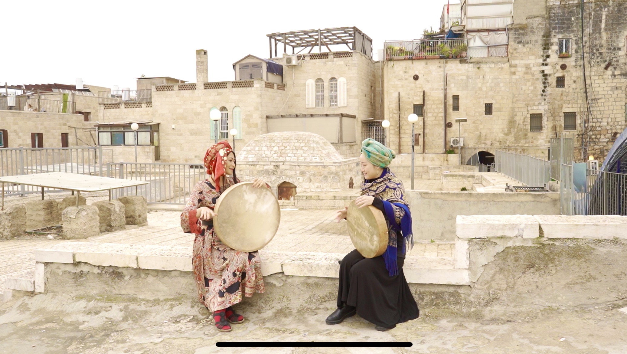 Ke Guo and Japanese musician Okaniwa Yayoi wearing bright traditional clothing and playing instruments in Jerusalem's Old City.