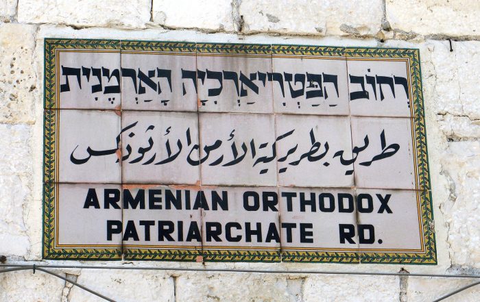 Tile sign embedded in a stone wall, with writing in Hebrew, Arabic, and English: "Armenian Orthodoc Patriarchate Rd."