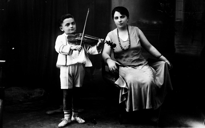 Black and white photo of mother in dress with young son and violin nearby