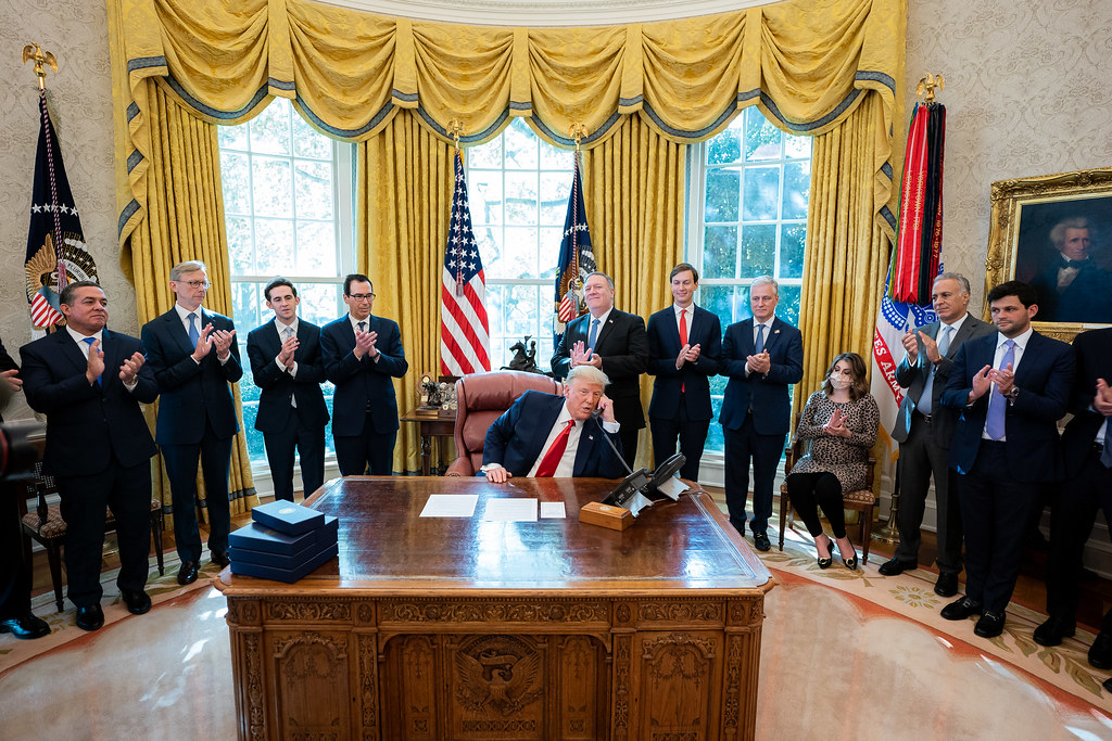 Men in suits applaud as Donald Trump speaks on phone in the Oval Office