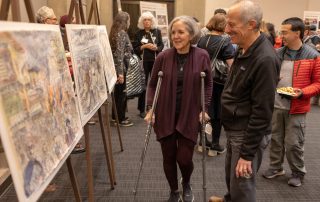 An older couple admiring Harry Naar's paintings at Muestros Artistas