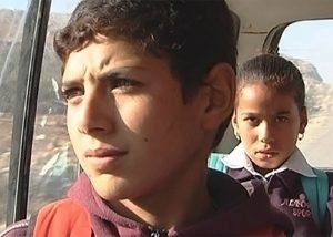 Child looks out window on a bus on dusty road