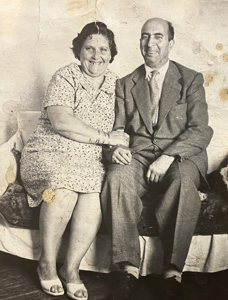 Black-and-white photo of a smiling couple in formalwear sitting on a couch