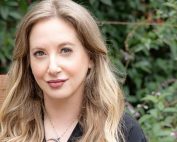 Leigh Bardugo, long hair over her shoulders, leaves in background