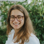 Woman wearing white shirt with glasses and long hair.