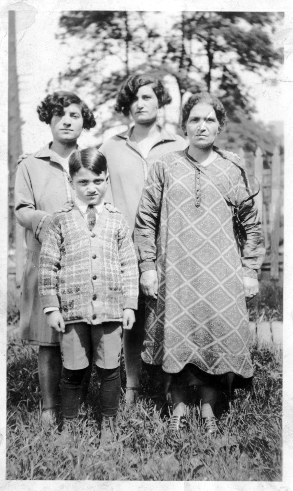 Black and white photo of middle-aged woman next with two young women and one boy outdoors in long coats