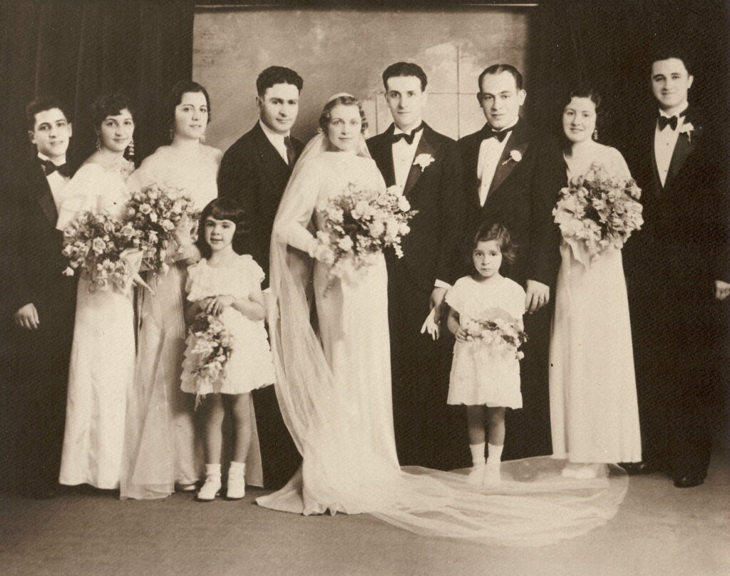 Portrait of wedding party with bride and groom in center, three bridesmaids with bouquets, four groomsmen, and two young flower girls in short dresses